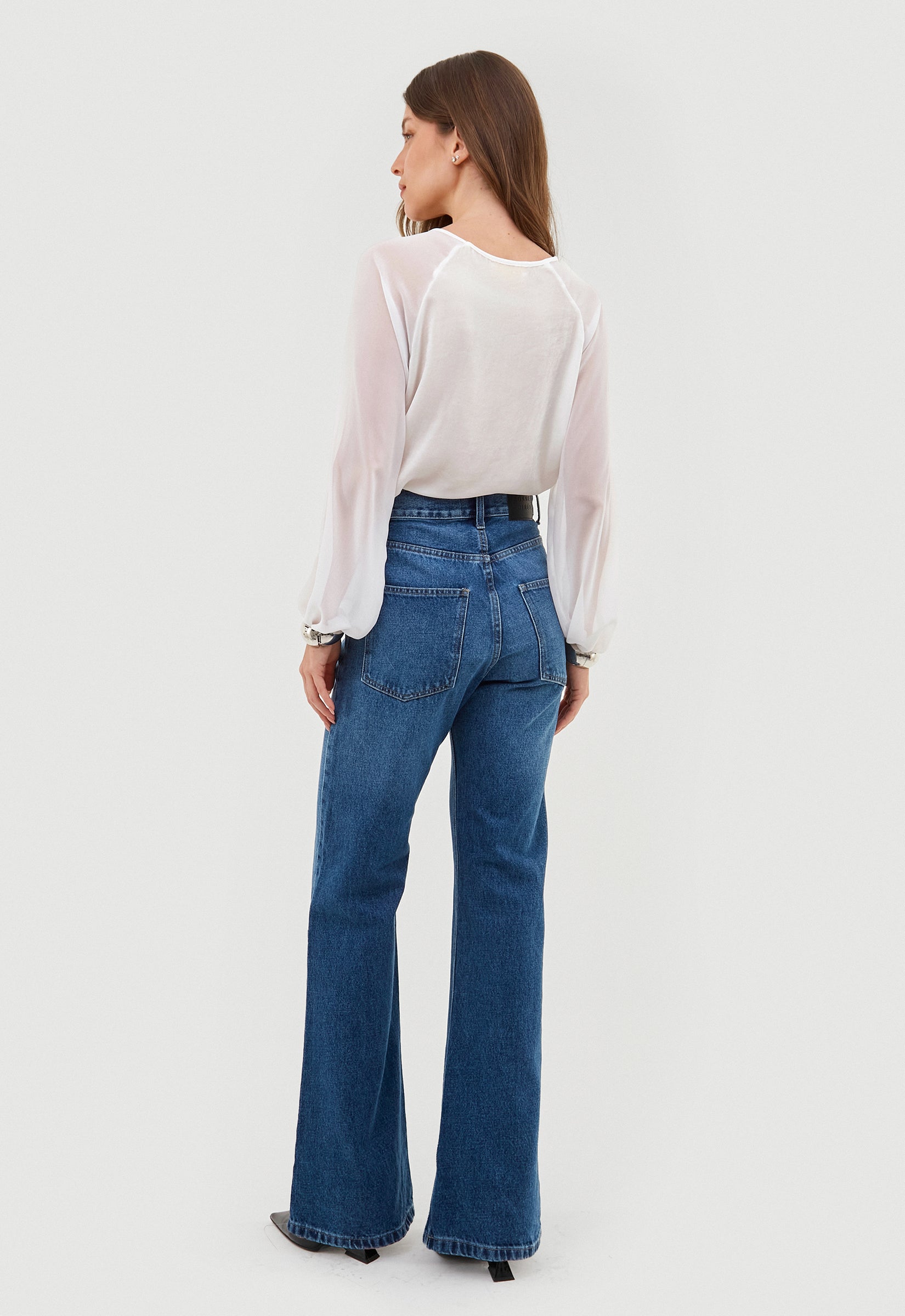 Modelo de costas usa calça jeans wide leg com blusa branca de manga longa