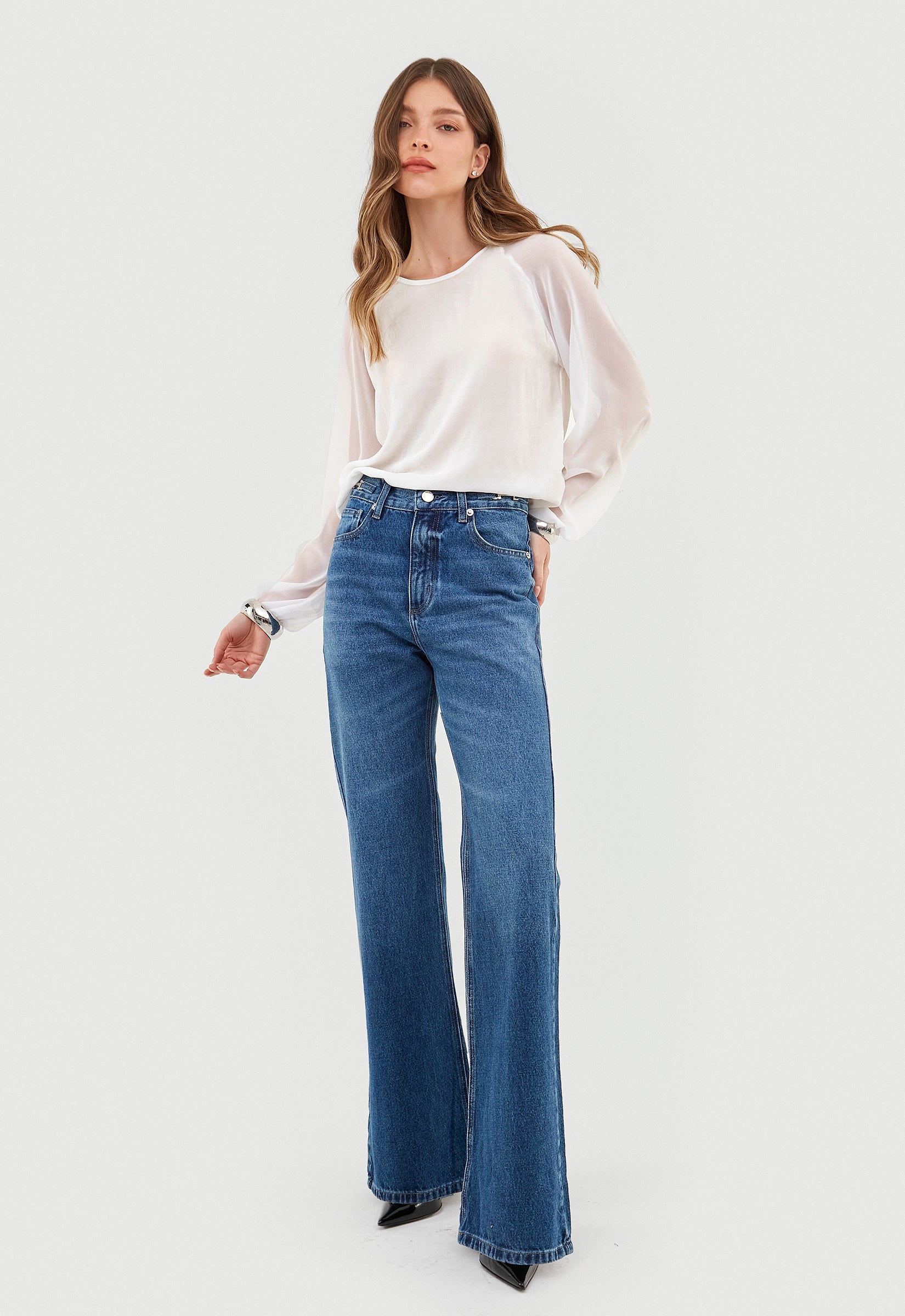 Modelo usa calça jeans wide leg azul com blusa branca de manga longa